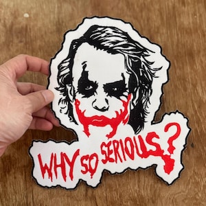 Pode incluir: Um remendo branco com uma imagem em preto e branco do Coringa do filme "O Cavaleiro das Trevas" com o texto "WHY SO SERIOUS?" em vermelho.