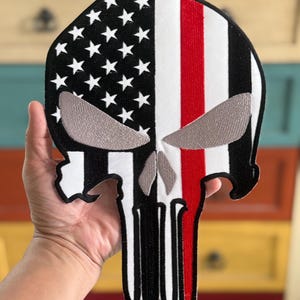 以下が含まれることがあります： 白と黒のアメリカ国旗が、右側に赤いストライプが入った、頭蓋骨の形をしている。頭蓋骨は白い輪郭と銀色の目をしている。