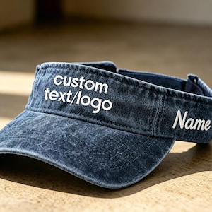 Könnte beinhalten: Ein blaues Denim-Visier mit weiß gesticktem Text "custom text/logo" und "Name". Das Visier schützt die Augen vor der Sonne und eignet sich für Outdoor-Aktivitäten.