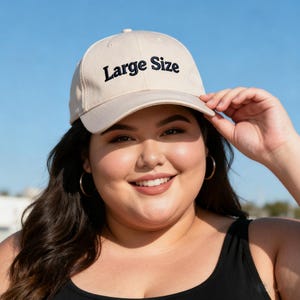 May include: A beige baseball cap with the words "Large Size" embroidered in black. The cap is worn by a person smiling. The background is a clear blue sky.