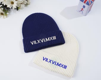 May include: Two knitted beanies, one navy blue and one white, with the Roman numeral inscription "VII.XVI.MXIII" on the front.