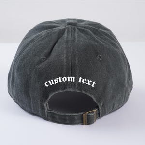 May include: A black baseball cap with a white embroidered text that says "custom text" in a gothic font.