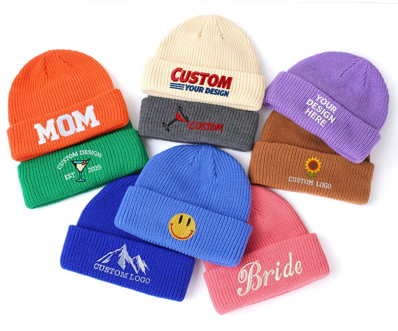 May include: A collection of eight knit beanies in orange, green, cream, dark gray, purple, brown, blue, and pink. Each beanie features embroidered text or graphics, including 'MOM', 'CUSTOM YOUR DESIGN', 'Bride', a smiley face, a mountain, and a sunflower.