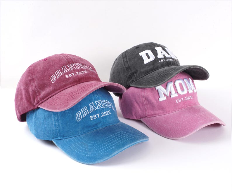 May include: Three baseball caps with different embroidered text. The first cap is red with "GRANDPA EST. 2025" in white. The second cap is blue with "GRANDPA EST. 2025" in white. The third cap is pink with "MOM EST. 2025" in white. The cap on top is black with "DAD EST. 2025" in white.