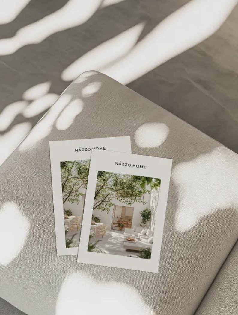 May include: Two white rectangular cards with the text "NAZZO HOME" on top. The cards feature a photograph of an outdoor patio with white furniture, trees, and sunlight. The cards are resting on a light gray surface.