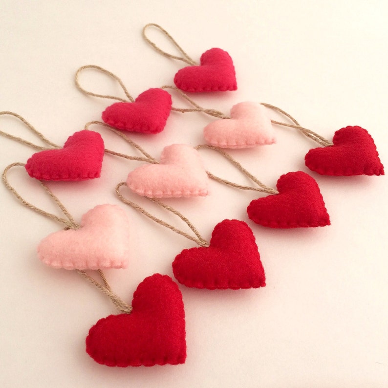 May include: A garland of felt hearts in shades of pink and red, each heart is attached to a twine string.