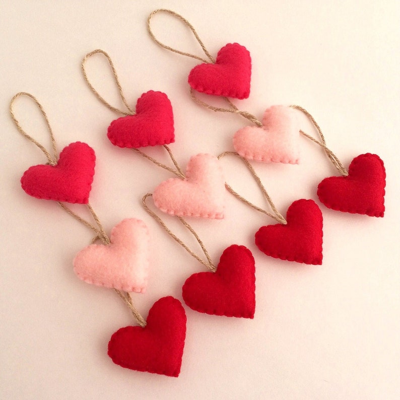 May include: A garland of felt hearts in pink and red, strung together with twine. The hearts are arranged in a alternating pattern, with the red hearts on top and the pink hearts on the bottom.