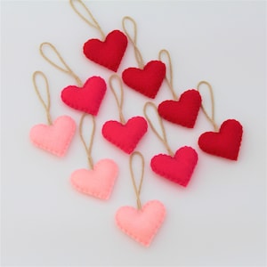 May include: Ten felt heart ornaments in shades of pink and red, each with a twine string for hanging.