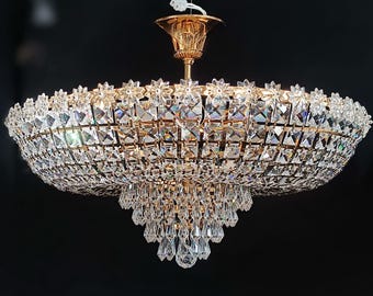May include: A large, ornate chandelier with a gold-colored frame and numerous crystal accents. The crystals are arranged in a tiered design, with a central cluster of hanging crystals. The chandelier is suspended from a white cord.