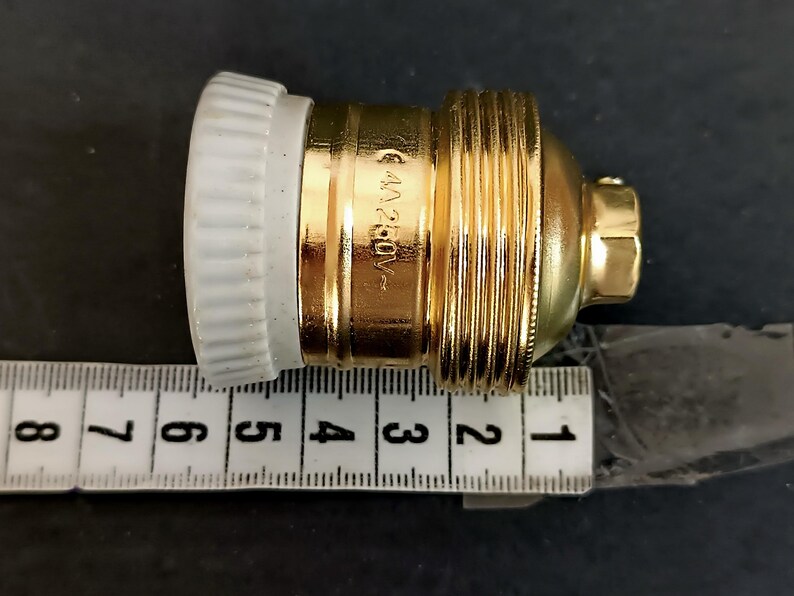 May include: A gold-coloured light bulb socket with a white ceramic base. The socket is 5 cm long and has a 6A 250V rating.