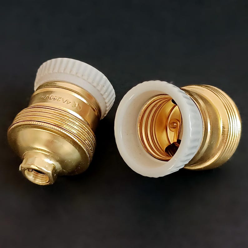 May include: Two gold-coloured light bulb sockets with white ceramic bases. The sockets have a threaded design and are marked with "CE" and "A/250V".