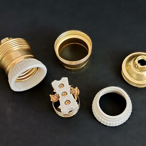 May include: A set of gold-toned electrical components for a light fitting. The set includes a ceramic socket, a ceramic base, a metal cap, and a metal connector.