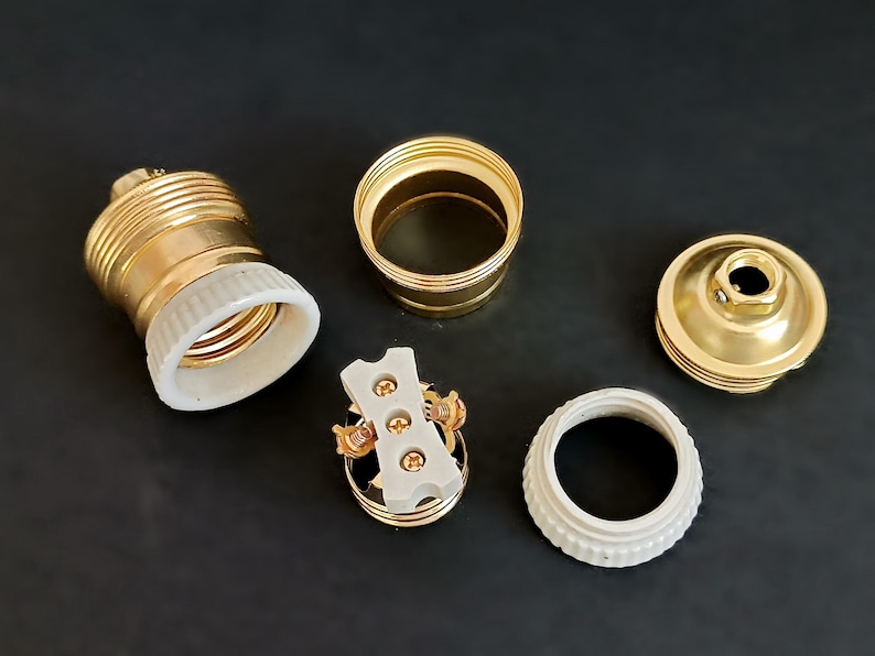 May include: A set of gold-toned electrical components for a light fitting. The set includes a ceramic socket, a ceramic base, a metal cap, and a metal connector.