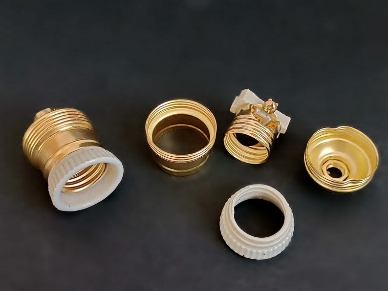 May include: Five gold-coloured light bulb sockets with white porcelain inserts. The sockets are in various stages of assembly.