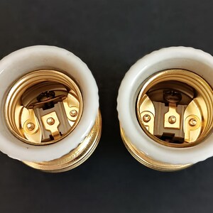 May include: Two white ceramic light bulb sockets with gold metal threads and a brass centre contact. The sockets are designed for standard light bulbs.