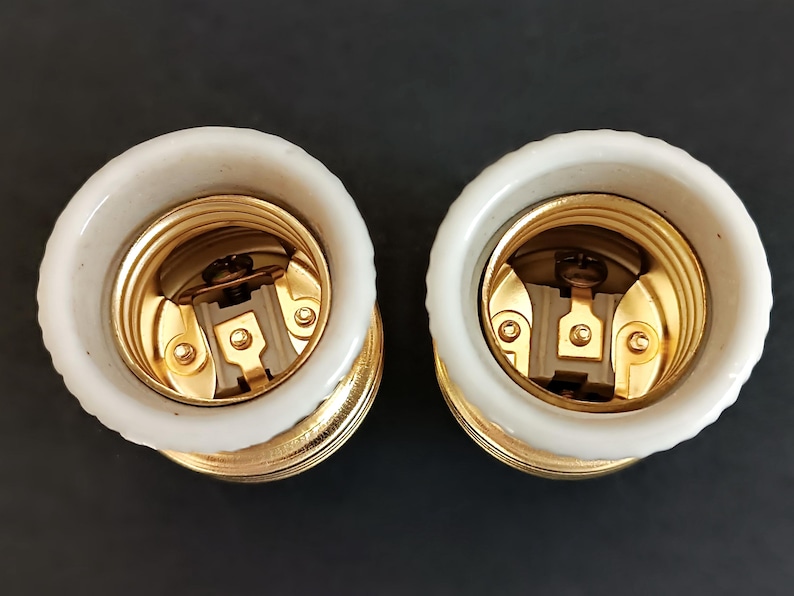 May include: Two white ceramic light bulb sockets with gold metal threads and a brass centre contact. The sockets are designed for standard light bulbs.
