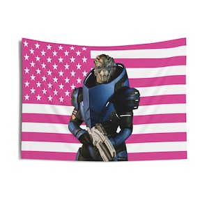 Puede incluir: Un tapiz con un personaje de la serie de videojuegos Mass Effect, sobre una bandera estadounidense rosa y blanca. El personaje está vestido con una armadura azul y sostiene un arma plateada. Las estrellas de la bandera son blancas.