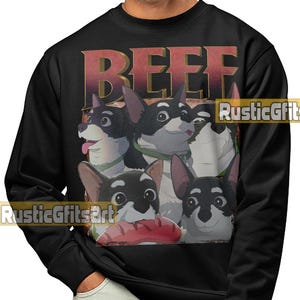 May include: Black sweatshirt featuring a graphic of four cartoon corgi dogs with the word "BEEF" in a distressed font. One dog holds a sausage. The sweatshirt has a crew neck and long sleeves.