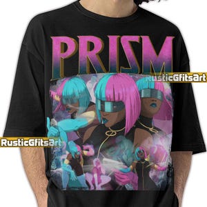 May include: Black t-shirt featuring a graphic design with the word "PRISM" in purple and gold. The design includes a stylized illustration of three women with blue and pink hair, wearing futuristic visors and outfits.