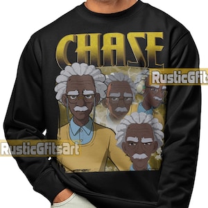 May include: Black sweatshirt featuring a graphic of a cartoon character with white hair, glasses, and a mustache. The word "CHASE" is printed in gold above the character. The character is wearing a yellow sweater and a blue collared shirt.