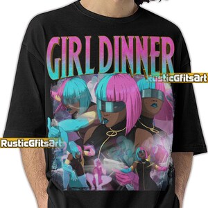 May include: Black t-shirt with a colourful graphic that reads "GIRL DINNER". The design features multiple figures with teal and pink hair, wearing futuristic visors and black outfits. The artist's name, "RusticGfitsArt", is also visible on the shirt.