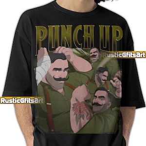 May include: Black t-shirt featuring a graphic of a man with a large mustache and a rose tattoo on his arm. The words "PUNCH UP" are printed in a gold color above the image. The image has a vintage, comic book style.