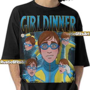 Op de afbeelding: Zwart t-shirt met een cartoon illustratie. Het ontwerp toont de tekst "GIRL DINNER" en een illustratie van een persoon met een blauwe bril en een geel en blauw jumpsuit. De naam van de kunstenaar "RusticGfitsArt" is ook zichtbaar.