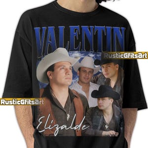 May include: Black t-shirt featuring a portrait of Valentin Elizalde with the text "VALENTIN" in blue and "Elizalde" in white. The design includes images of the singer wearing a cowboy hat.