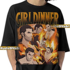 May include: Black t-shirt with a graphic featuring multiple male figures in a fiery background, with the text "GIRL DINNER" in a gold, distressed font. The artist's name "RusticGfitsArt" is also visible.