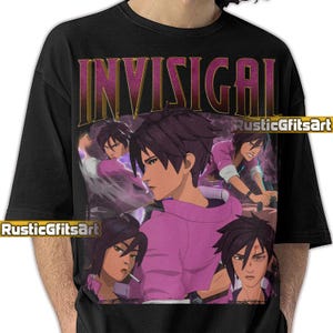 May include: Black t-shirt with a graphic design featuring the word "INVISIGAL" in gold lettering. The design includes multiple images of a person in a pink hoodie. The artist's name, "RusticGfitsArt," is also visible.
