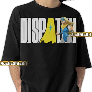 May include: Black t-shirt with the word "DISPATCH" in large white letters. A superhero graphic is on the right side, featuring a blonde woman in a blue and yellow costume. The shirt also has the text "RusticGiftsArt".