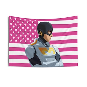 May include: A wall tapestry featuring an illustration of a superhero in a gray and orange suit, with a black helmet, standing in front of a pink American flag. The flag has white stars and pink stripes. The superhero has their arms crossed.
