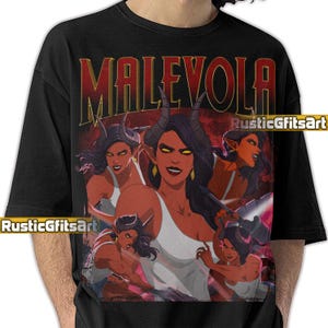 May include: Black t-shirt featuring a graphic of a woman with horns, red skin, and yellow eyes. The word "MALEVOLA" is printed in red above the image. The shirt has the text "RusticGfitsArt" printed on it.