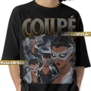 May include: Black t-shirt featuring a graphic of a woman wearing a silver mask, with the word "COUPÉ" in large, metallic letters. The design includes multiple images of the woman in a black outfit. The artist's name "RusticGiftsArt" is also visible.