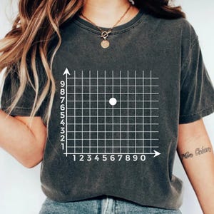 May include: Dark gray t-shirt featuring a white grid with numbered axes and a white dot at the coordinates (6, 6). The shirt is made of a soft material.