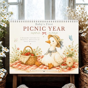 May include: A spiral-bound calendar titled Baby's First PICNIC YEAR featuring a white duck wearing a straw hat and blue checkered scarf. The illustration includes a wicker basket of strawberries, a red checkered blanket, and wildflowers.