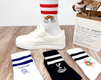 May include: Three pairs of colorful striped socks with different embroidered designs. One pair is white with red stripes and a rainbow design, another is white with blue stripes and a tennis racket design, and the last pair is black with white stripes and a cocktail glass design.