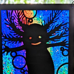 May include: Axolotl suncatcher made from clear acrylic and painted black MDF. The suncatcher features a black silhouette of an axolotl with rainbow iridescent details.