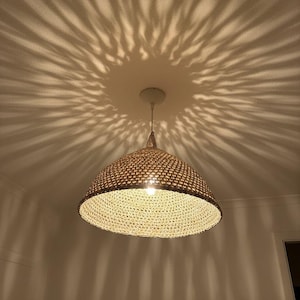 May include: A woven pendant light fixture with a conical shade. The light casts a starburst pattern on the ceiling. The fixture is suspended from a white ceiling mount. The shade is a light brown color.