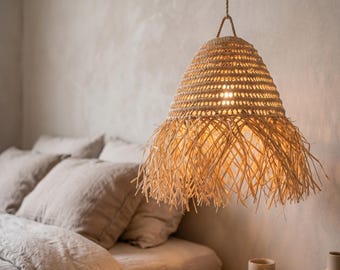 May include: A hanging pendant light fixture featuring a woven, conical shade made of natural tan fibers. The upper section has a tight, structured weave, while the lower edge is finished with a long, loose fringe of thin, straw-like strands.