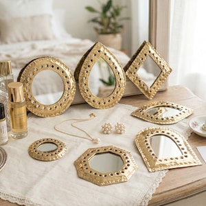 Puede incluir: Una colección de espejos decorativos dorados de varias formas, incluyendo redondos, de lágrima y de diamante, dispuestos sobre una superficie de madera. Los espejos están rodeados de pequeños agujeros decorativos. También hay joyas, frascos de perfume y un port anillos.