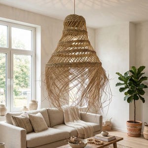 Puede incluir: Una gran lámpara colgante tejida cuelga sobre un sofá beige en una sala de estar. La lámpara está hecha de fibras naturales y tiene forma de campana. La habitación también cuenta con una mesa de centro de madera, una planta en maceta y una ventana.