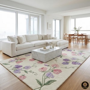 Könnte beinhalten: Ein cremefarbener Teppich mit einem Blumendesign aus rosa und lila Platterbsenblüten und grünen Stielen. Der Teppich befindet sich in einem Wohnzimmer mit einem weißen Ecksofa und einem Marmor-Couchtisch. Der Raum hat große Fenster und Holzböden.