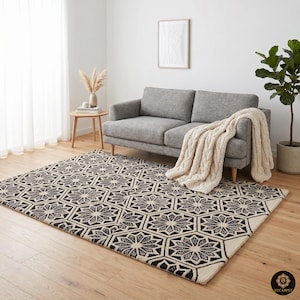 May include: A rectangular area rug featuring a repeating geometric pattern of black and cream-colored star-like shapes within hexagonal outlines. The rug is laid flat on a light-colored wooden floor, showcasing a high-contrast, symmetrical design.