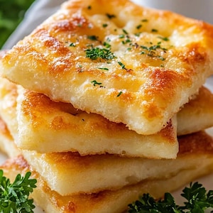 Könnte beinhalten: Ein Stapel von vier goldbraunen, knusprigen Fladenbroten, garniert mit frischer Petersilie, auf einem weißen Teller.