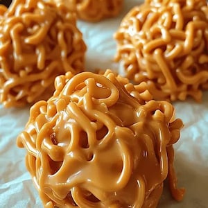 May include: Close-up of four peanut butter balls covered in a caramel-like coating. The balls are arranged on a white parchment paper background.