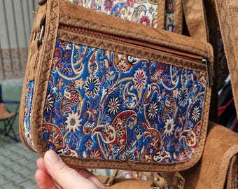 Pode incluir: Uma bolsa de couro marrom transversal com um padrão floral azul e vermelho. A bolsa tem um fecho de zíper e uma aba.