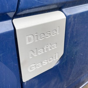 May include: A grey fuel cap with the words "Diesel", "Nafta", and "Gasoil" printed on it. The cap is attached to a blue vehicle.