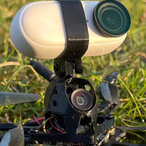 Könnte beinhalten: Ein schwarzer 3D-gedruckter Kamerahalter mit einer weißen Kamera, die daran befestigt ist. Die Kamera hat ein schwarzes Objektiv und ist auf einer Drohne montiert.