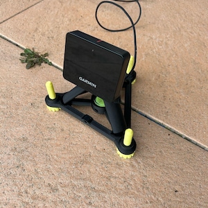 Könnte beinhalten: Eine schwarze Garmin-Kamera, die auf einem Stativ mit gelben Beinen montiert ist. Die Kamera ist mit einem schwarzen Kabel verbunden.
